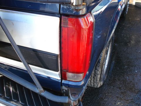 1994 Ford Bronco - Close-up of a blue truck's rear section, showing the tail light and a silver trim panel.