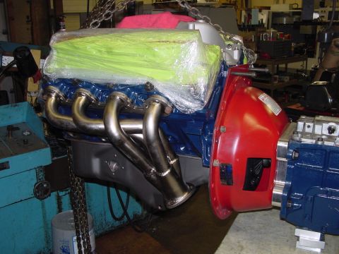 1979 Ford Bronco - Engine assembly with custom headers and a red bell housing, suspended by chains in a workshop.