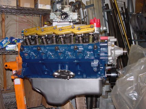1979 Ford Bronco - A blue V8 engine with gold valve covers and a red distributor cap is mounted on an orange engine stand in a workshop.