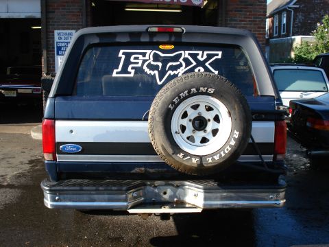 1994 Ford Bronco - Rear view of a blue Ford Bronco with a spare tire and a Fox logo sticker on the rear window.