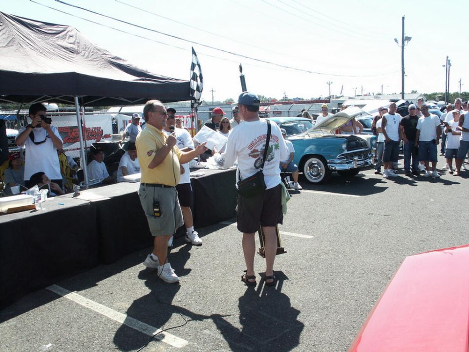 Blue classic car with hood open, front view. People gathered around