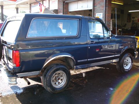 1994 Ford Bronco - Side view of a dark blue 1994 Ford Bronco parked in front of a brick building.