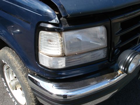 1994 Ford Bronco - Close-up of a dark blue Ford Bronco's front end, showing a cracked headlight and chrome bumper.