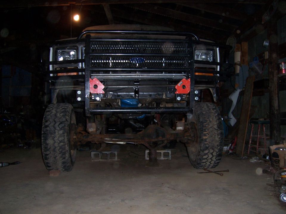 Front view of a lifted Ford Bronco with a brush guard and aftermarket grille. It's in a garage