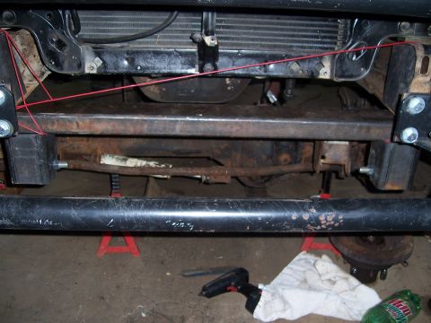 1983 Ford Bronco - The vehicle's front end is supported by jack stands, showing the crossmember and suspension parts.