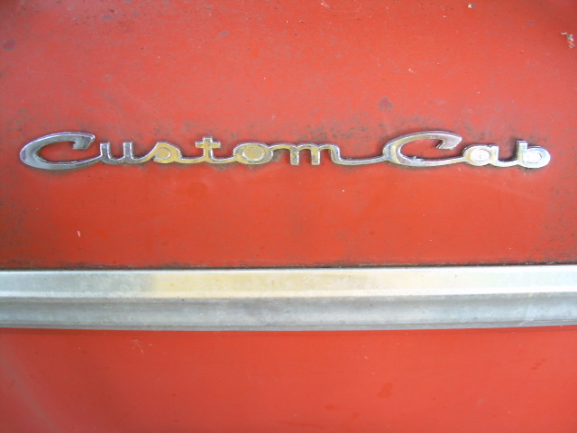 Chrome 'Custom Cab' script emblem on a faded red-orange truck panel