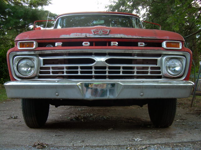 Front view of faded red 1960s Ford pickup with FORD grille letters and chrome bumper