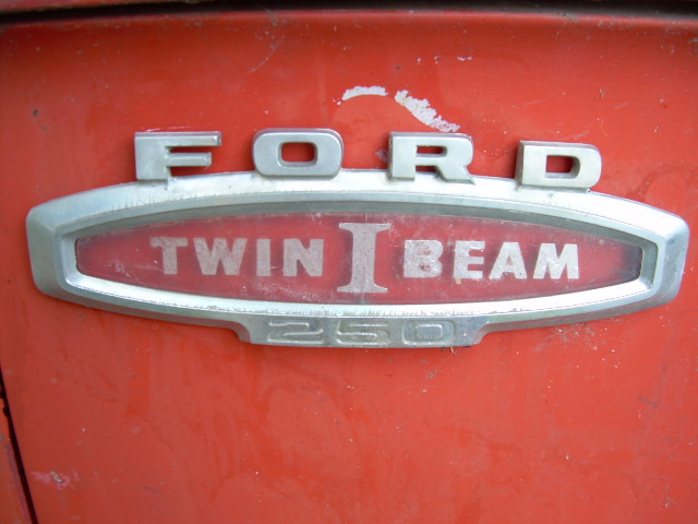 Close-up of FORD Twin I Beam 250 chrome fender emblem on faded red panel