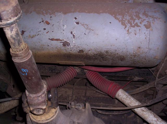 Underside view of a driveshaft and fuel tank with red bellows hoses