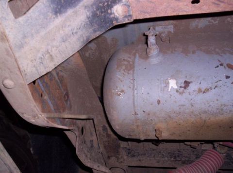1995 Ford Bronco - The underside of a vehicle reveals a large cylindrical fuel tank and rusted frame components.