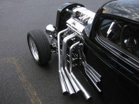 1979 Ford Bronco - A black hot rod displays its chrome engine and exhaust pipes from a three-quarter front view.