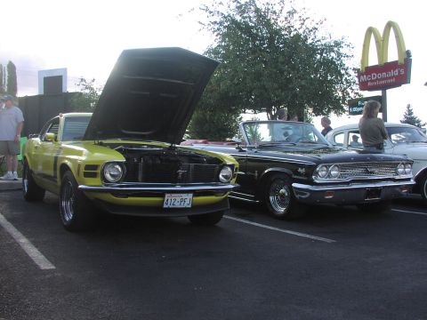 1979 Ford Bronco - A yellow 1970 Ford Mustang Mach 1 is parked with its hood open next to a black convertible, with a McDonald's sign in the background.