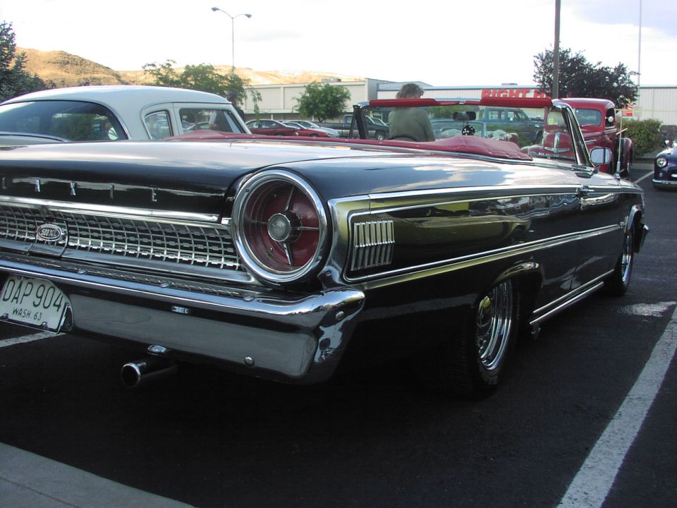 Black 1963 Ford Galaxie convertible with red interior, parked in a lot. Other cars are visible in the background