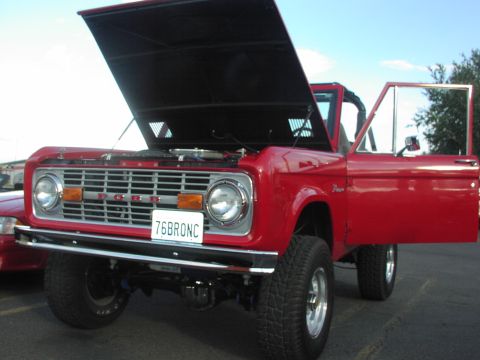 1979 Ford Bronco - A red 1976 Ford Bronco is shown with its hood and driver's door open, revealing the engine bay.