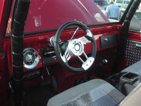1979 Ford Bronco - The interior of a red SUV features a custom steering wheel and plaid seat covers.