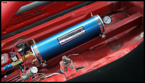 1993 Ford Mustang - Close-up of a blue Accusump air suspension tank and associated plumbing within a red-painted vehicle compartment.