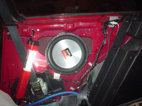 1995 Ford Probe - A car's interior door panel is removed to reveal a Polk Audio subwoofer and associated wiring, along with a seatbelt mechanism.