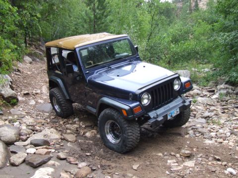 1997 Jeep TJ - This blue 1997 Jeep TJ navigates a challenging rocky path, demonstrating its off-road capabilities.