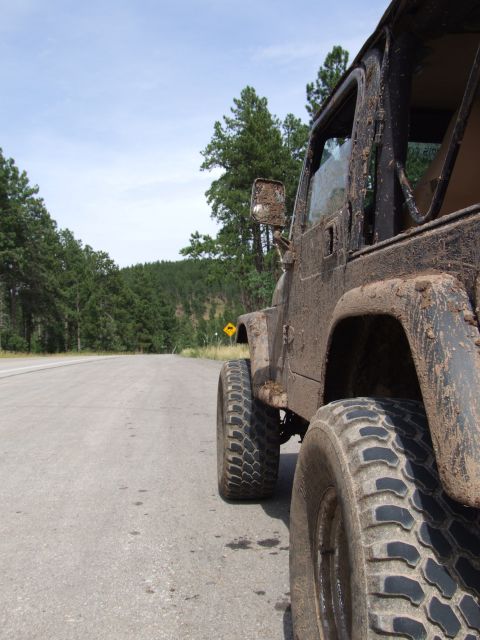 1997 Jeep TJ - Muddy 1997 Jeep TJ parked on the side of a road, with trees and a yellow warning sign visible.