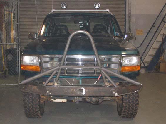 Dark green Ford Bronco front view with raw steel bumper and tube grille guard in shop