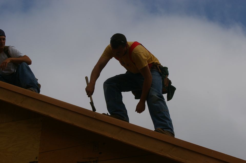 Two guys working on a roof, one is hammering and the other is sitting
