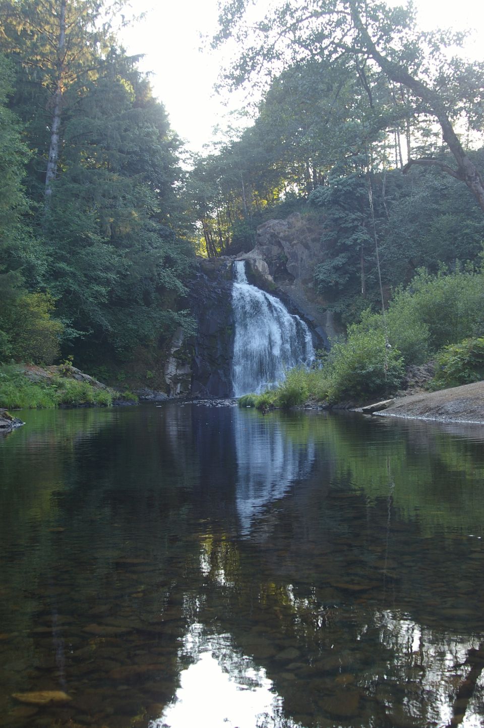 Waterfall cascading into a calm river with reflections of trees and sky