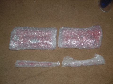 1995 Ford Probe - Four red car parts are individually wrapped in bubble wrap and laid out on a carpeted surface.