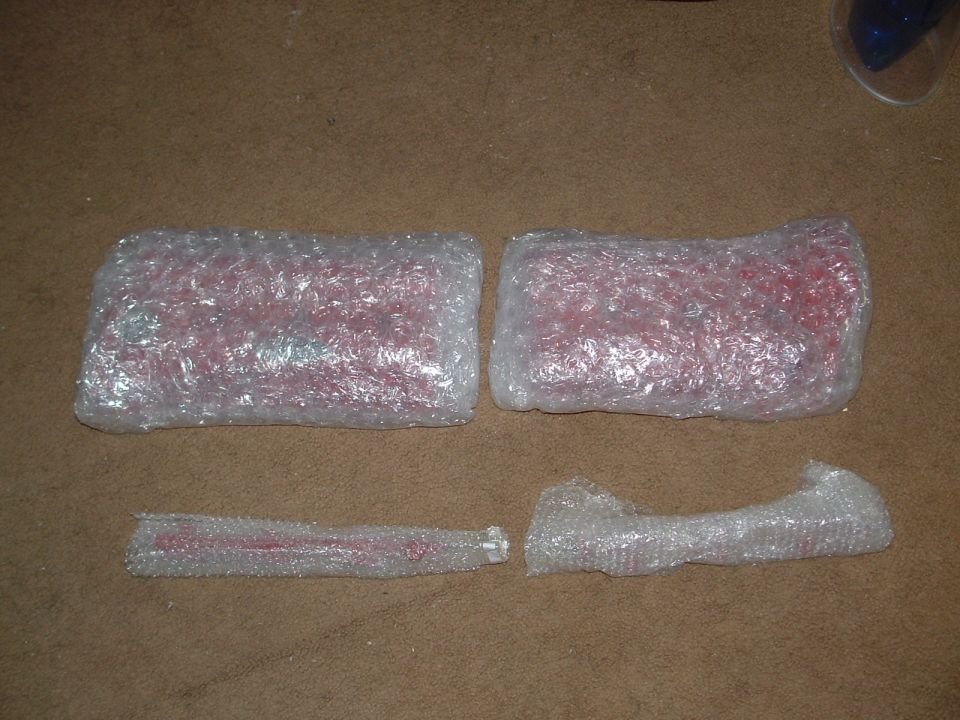 Four red car parts wrapped in bubble wrap on a brown carpeted surface