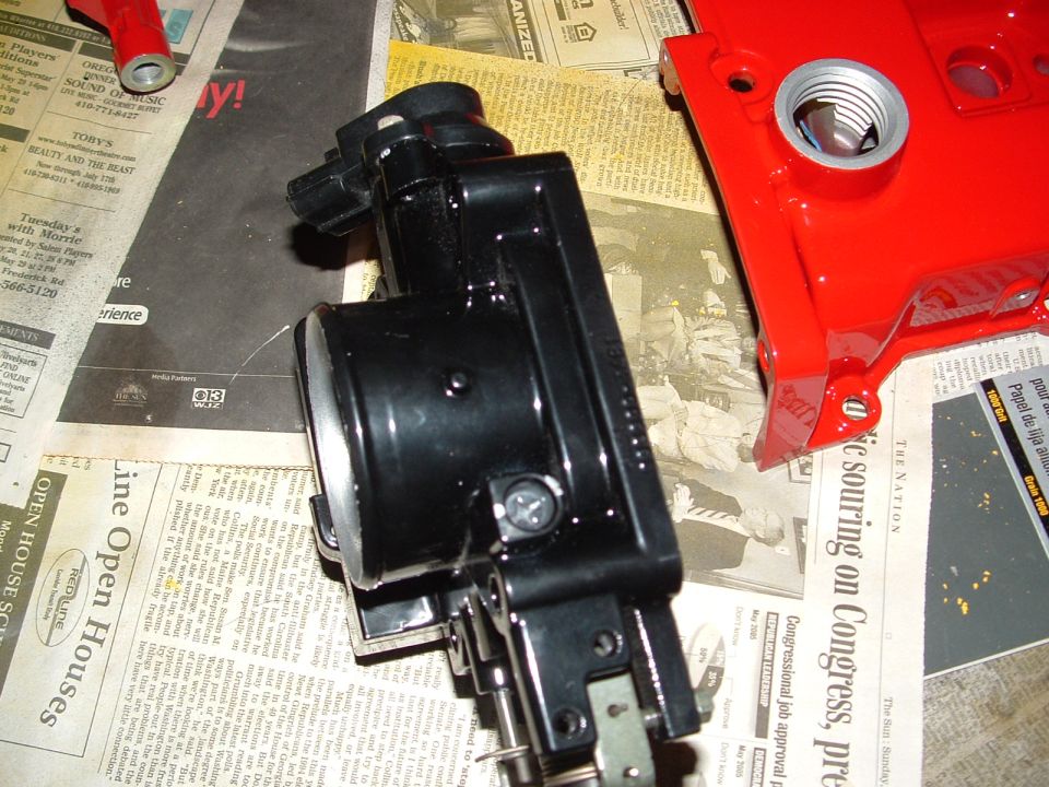 Black throttle body and red valve cover on newspaper