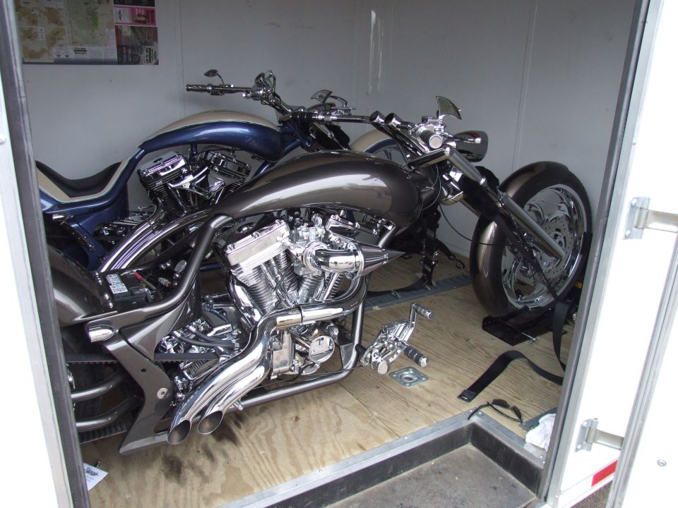 Two custom motorcycles, one dark gray and one blue and white, parked inside a trailer