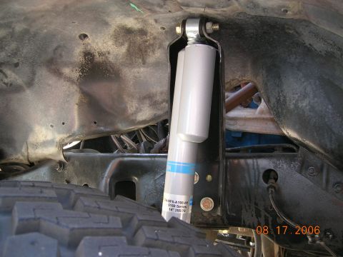 1985 Ford Bronco - A close-up view shows a silver Bilstein shock absorber with blue bands, mounted near a tire, with visible chassis components.