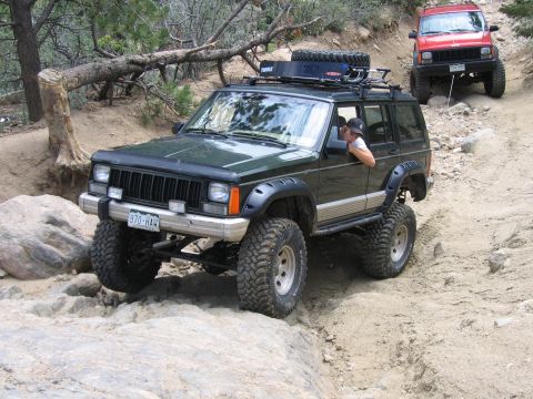 1996 Jeep Cherokee - Two Jeep Cherokees tackle a challenging off-road trail with steep inclines and rocky terrain.
