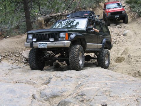 1996 Jeep Cherokee - Two modified Jeeps navigate a rocky off-road trail, with the lead vehicle showing significant suspension lift and large tires.