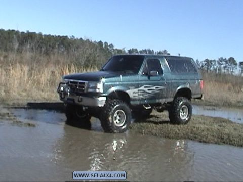 1995 Ford Bronco - A green Ford Bronco with flame decals navigates through a muddy terrain.