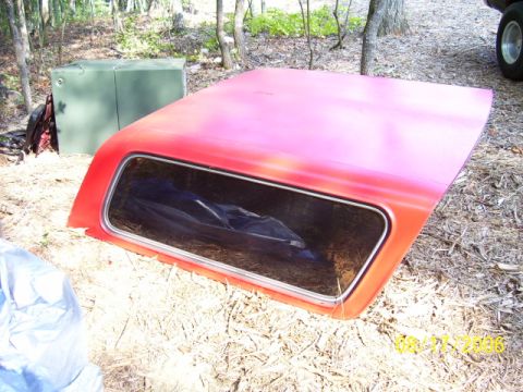 1979 Ford Bronco - Red truck cap with a window, resting on the ground in a wooded area.