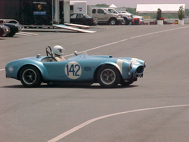 Light blue Shelby Cobra roadster number 142 with driver on pit lane