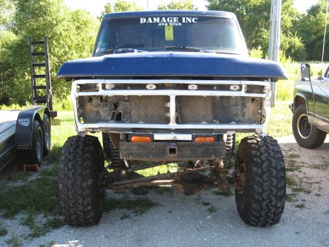 1977 Ford F-150 - A blue 1977 Ford F-150 is shown from the front, missing its grille and with large off-road tires.