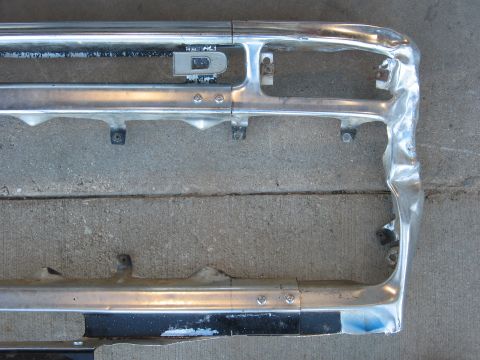 1977 Ford F-150 - A damaged chrome grille, likely from a truck, lies on a concrete surface.