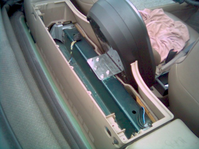 Disassembled tan center console showing green transmission tunnel with aluminum bracket and wiring