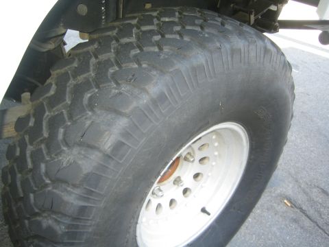 1990 Ford Bronco - worn mud-terrain tire mounted on a white steel wheel sits under a vehicle's fender on pavement.