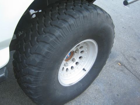 1990 Ford Bronco - aggressive mud-terrain tire on a white steel wheel mounted to a white vehicle, shot at the wheel well.
