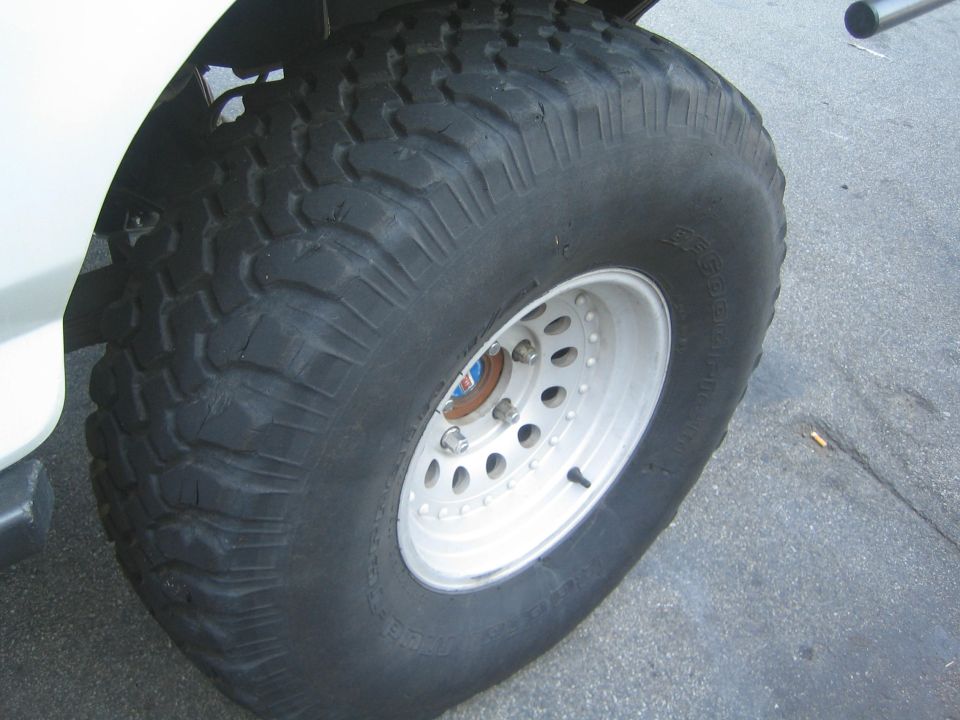 Aggressive mud-terrain tire on white steel wheel against white vehicle body
