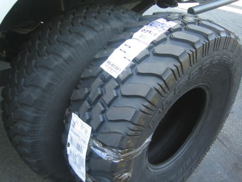 1990 Ford Bronco - New mud-terrain tires bearing white paper price labels stacked beside a vehicle's wheel well.
