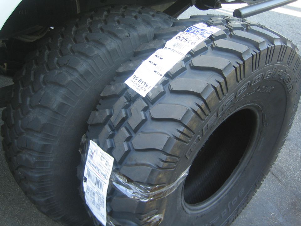 New mud-terrain tires with paper labels stacked by a vehicle fender