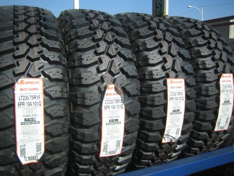 1990 Ford Bronco - row of new Summit Mud Dawg LT235/75R15 mud-terrain tires standing on a rack with paper spec labels.