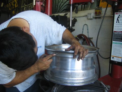 1990 Ford Bronco - man in a gray shirt leans over a bare aluminum alloy wheel rim mounted on a shop tire machine.