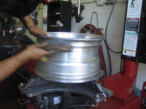 1990 Ford Bronco - bare aluminum alloy wheel rim sits on a red tire-changing machine as a hand brushes its surface.