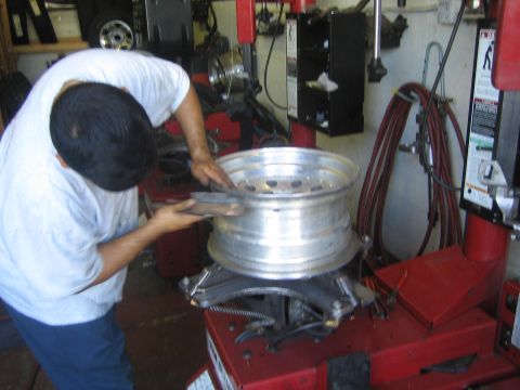 1990 Ford Bronco - man in a white shirt works a bare steel wheel mounted on a red tire-changing machine in a tire shop.
