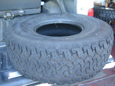 1990 Ford Bronco - large worn all-terrain tire and wheel lie flat on a vehicle's open tailgate or bed.