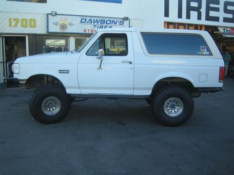 1990 Ford Bronco - Side profile of a lifted white Ford Bronco fitted with a camper top, parked in front of Dawson's Tires.